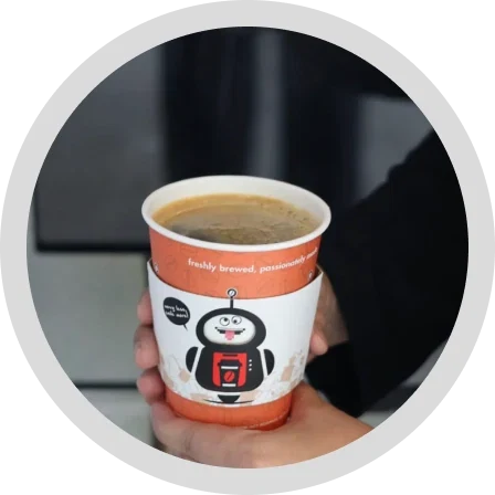 A hand holding a freshly brewed CoffeeBot cup in front of a machine.
